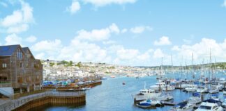 Perché visitare Falmouth: l’anima marittima della Cornovaglia Veduta panoramica del porto storico di Falmouth in Cornovaglia, con numerose barche a vela e imbarcazioni ormeggiate in un'ampia baia naturale sotto un cielo sereno.